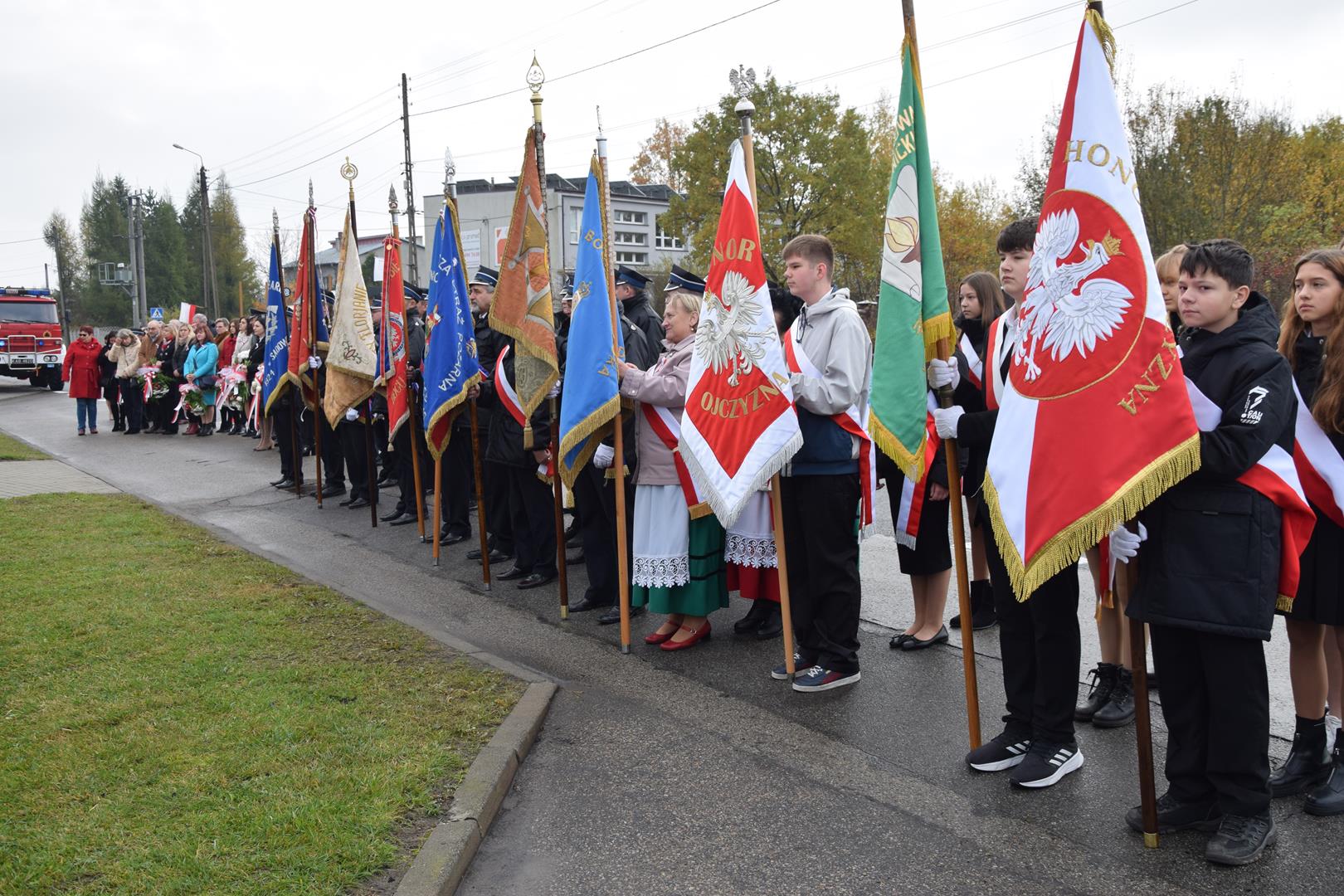 Zdjęcie przedstawia ludzi stojących ze sztandarami