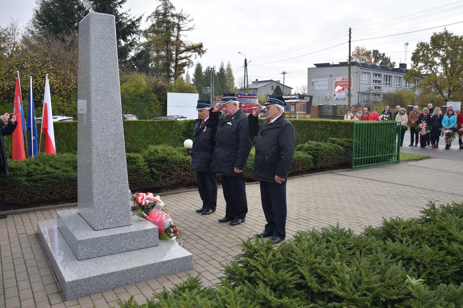 Zdjęcie przedstawia moment składania kwiatów przed pomnikiem przez reprezentantów jednostek pożarniczych
