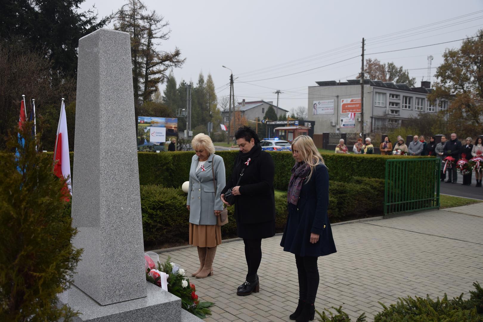 Zdjęcie przedstawia moment wręczenia kwiatów pod pomnikiem