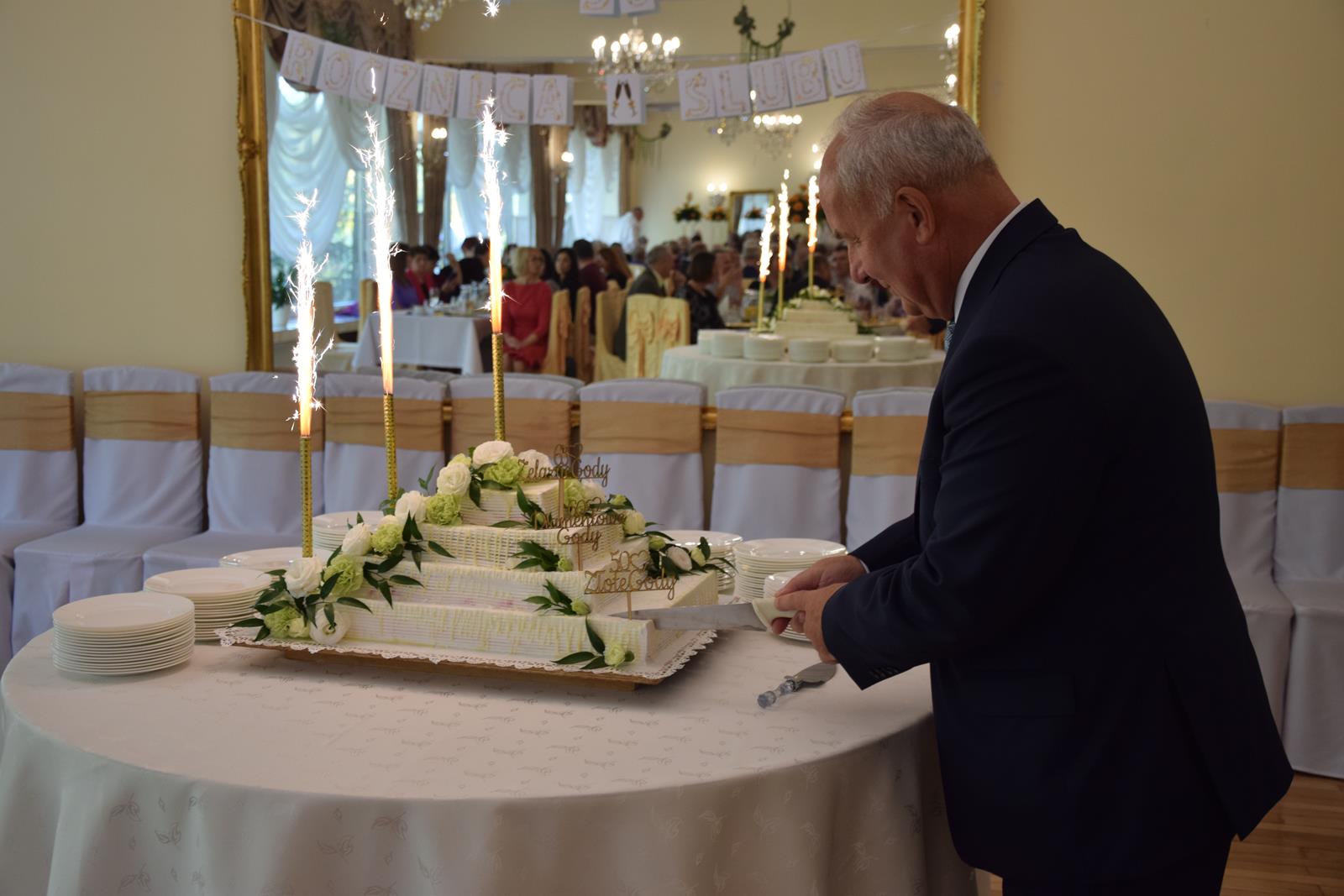 Zdjęcie przedstawiające wójta gminy rozpoczynającego sybliczne krojenie tortu