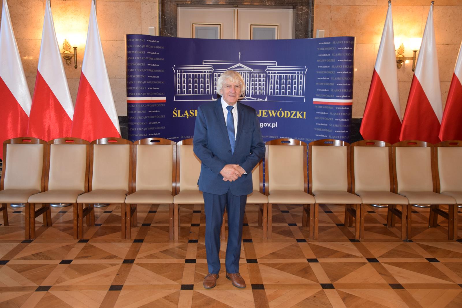 Zdjęcie - pan Józef Kotuła w Śląskim Urzędzie Wojewódzkim na tle flag Polski
