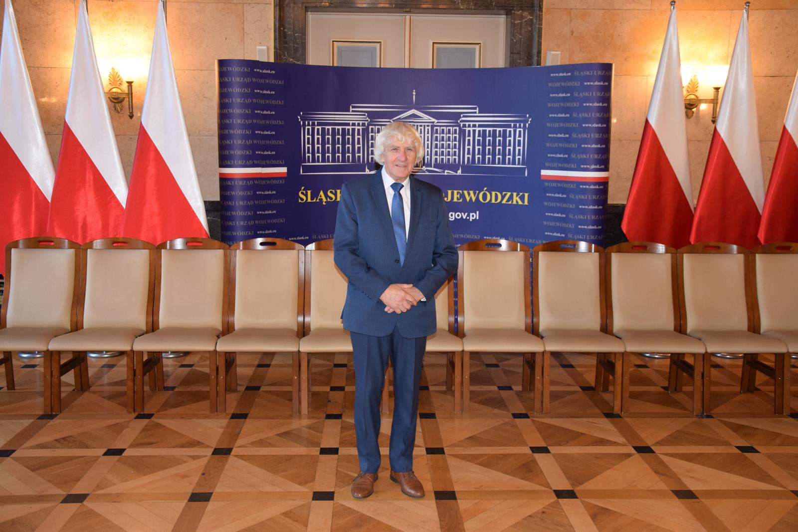 Zdjęcie - pan Józef Kotuła w Śląskim Urzędzie Wojewódzkim na tle flag Polski
