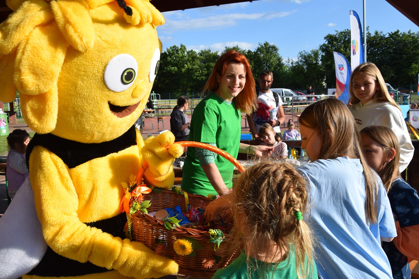 Zdjęcie przedstawia maskotkę pszczołę rozdającą podarki dzieciom na pikniku ekologicznym