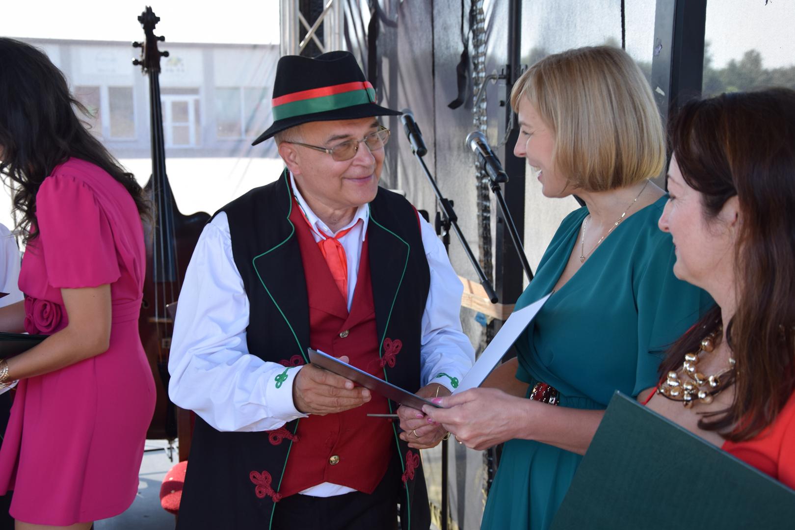 Zdjęcie przedstawia moment wręczania pamiątkowych dyplomów i nagród dla gości zaproszonych na Jubileusz Kapeli