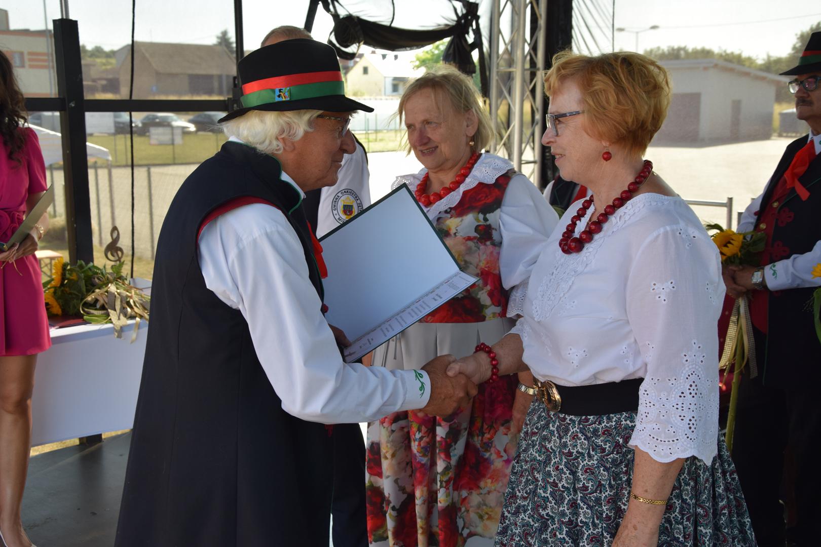 Zdjęcie przedstawia moment wręczania pamiątkowych dyplomów i nagród dla gości zaproszonych na Jubileusz Kapeli