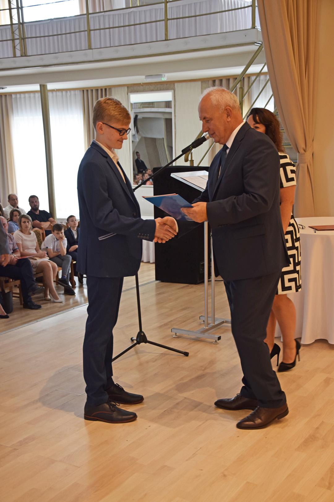 Zdjęcie przedstawia ucznia odbierającego nagrodę wójta