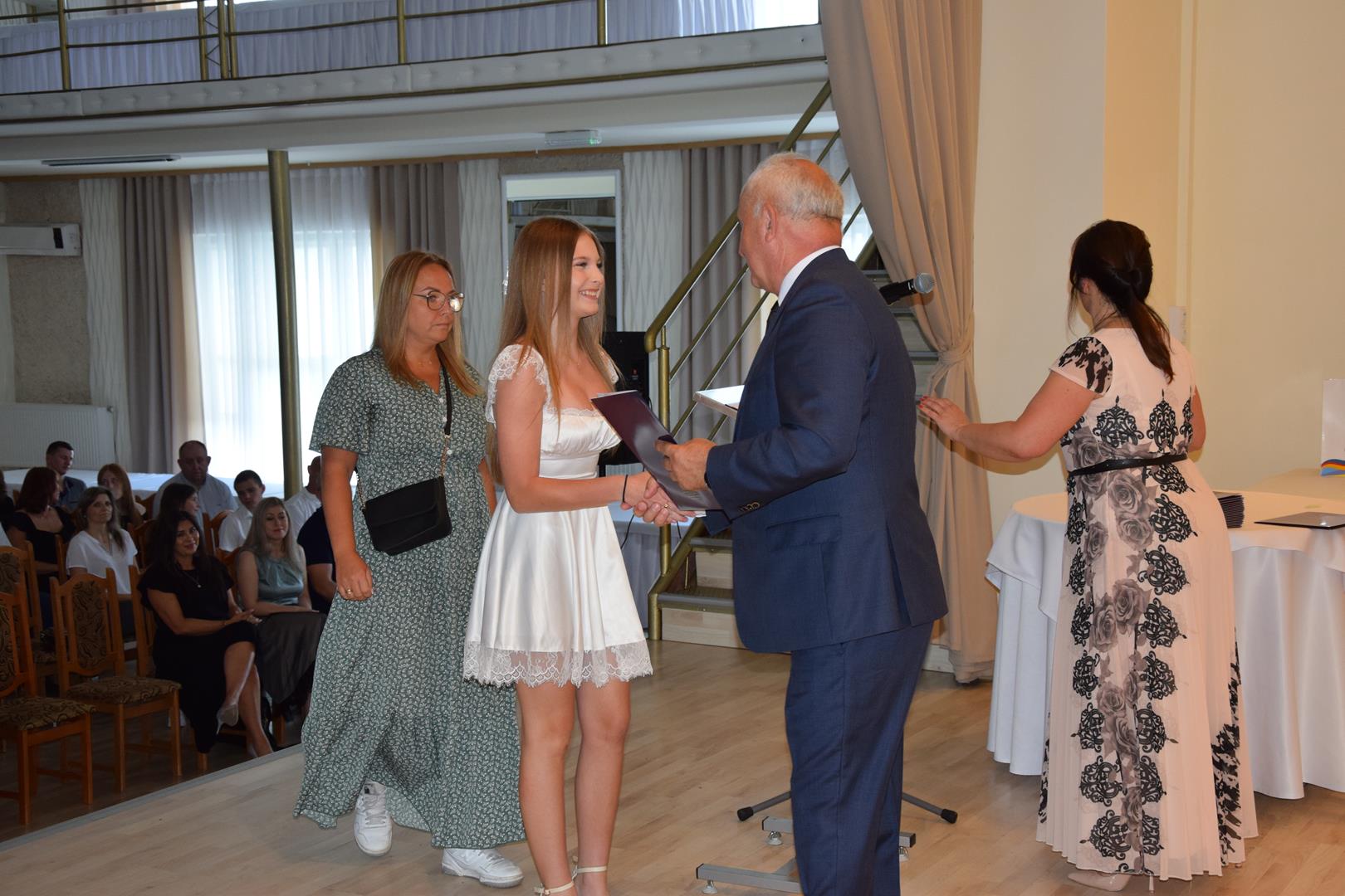 Zdjęcie przedstawia moment wręczenia dyplomów z okazji promocji ucznia zdolnego 2024