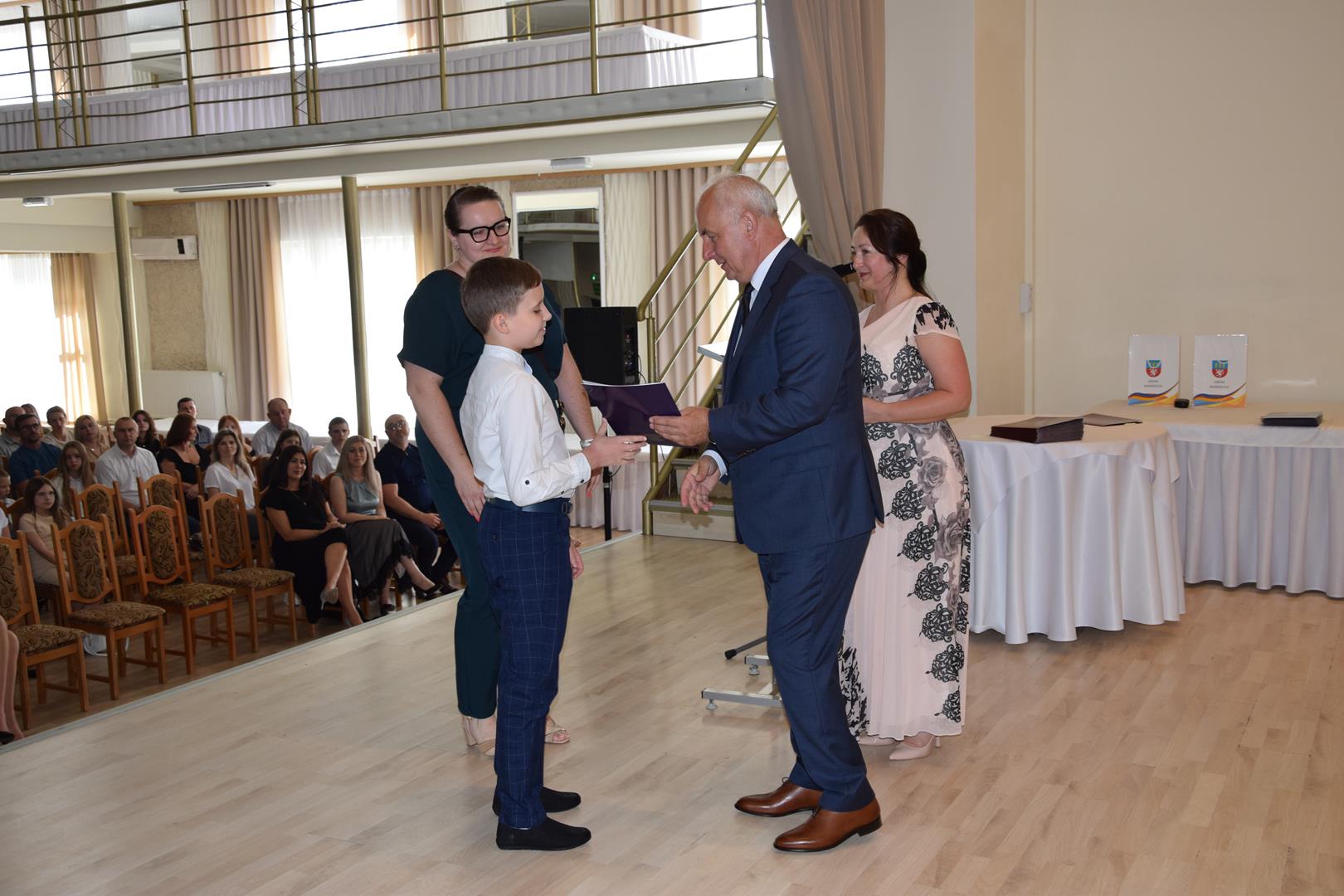 Zdjęcie przedstawia moment wręczenia dyplomów z okazji promocji ucznia zdolnego 2024