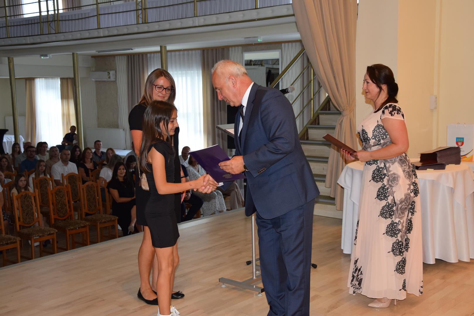 Zdjęcie przedstawia moment wręczenia dyplomów z okazji promocji ucznia zdolnego 2024