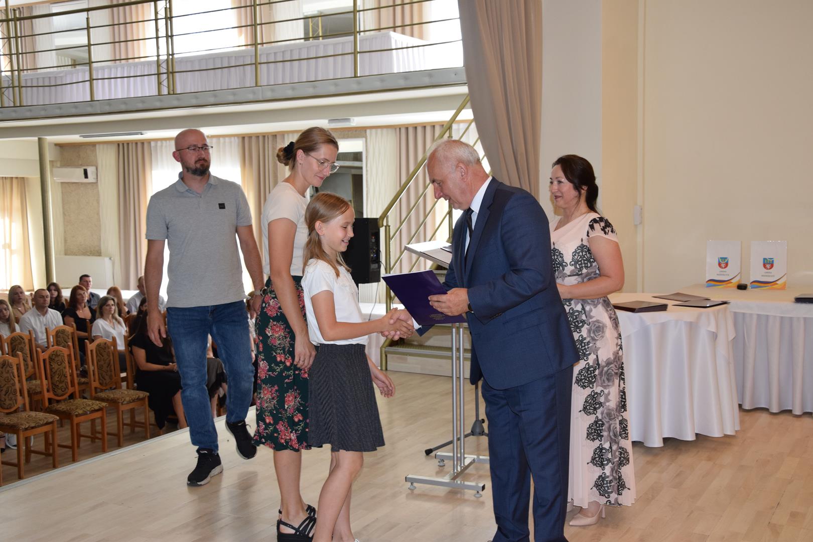 Zdjęcie przedstawia moment wręczenia dyplomów z okazji promocji ucznia zdolnego 2024