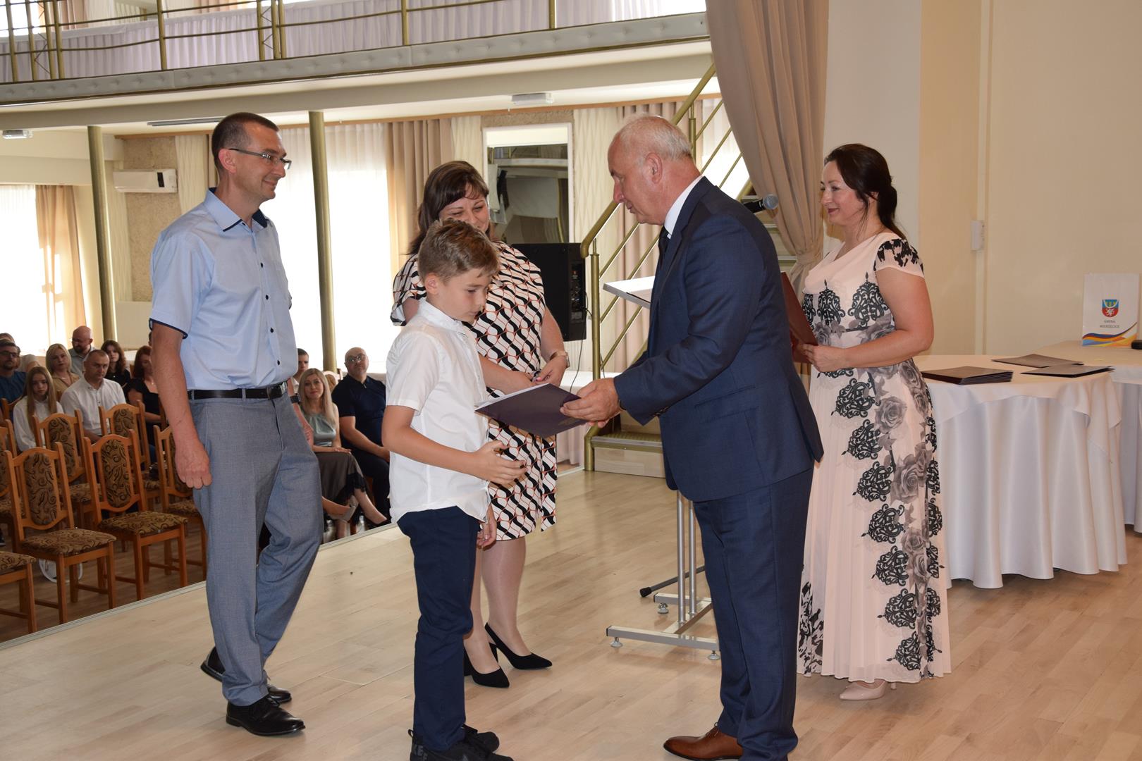Zdjęcie przedstawia moment wręczenia dyplomów z okazji promocji ucznia zdolnego 2024