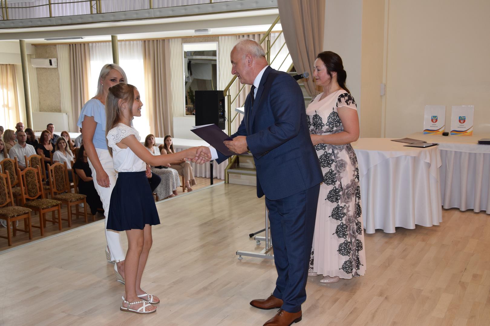 Zdjęcie przedstawia moment wręczenia dyplomów z okazji promocji ucznia zdolnego 2024