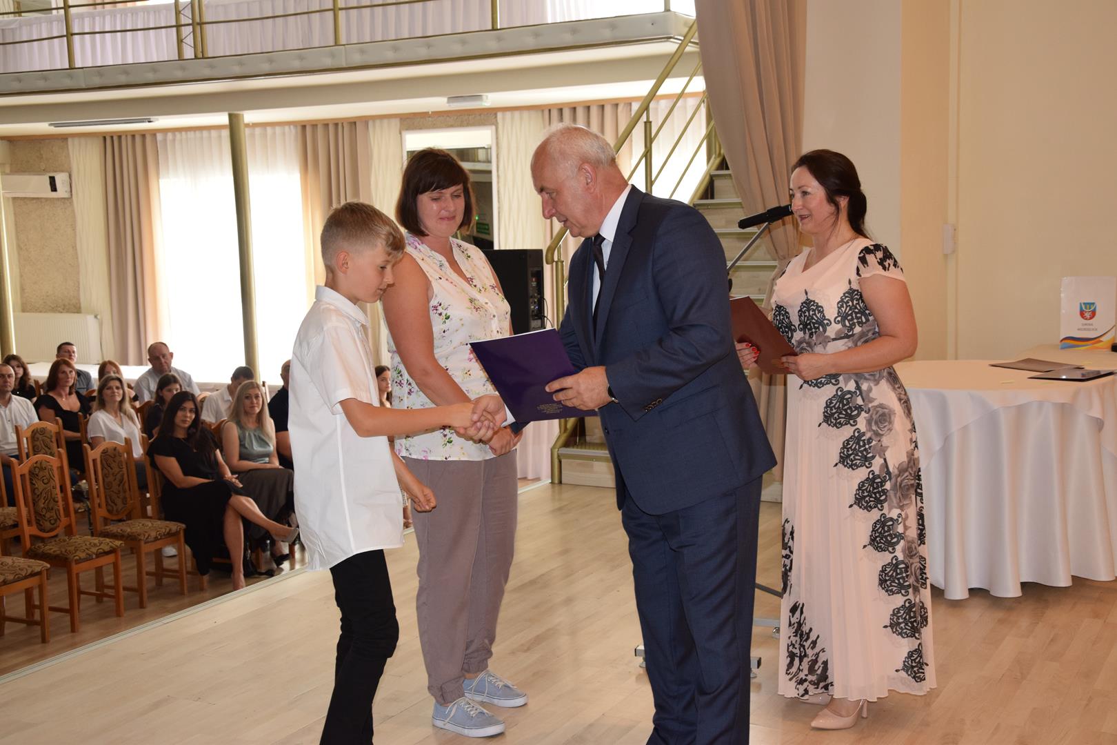 Zdjęcie przedstawia moment wręczenia dyplomów z okazji promocji ucznia zdolnego 2024