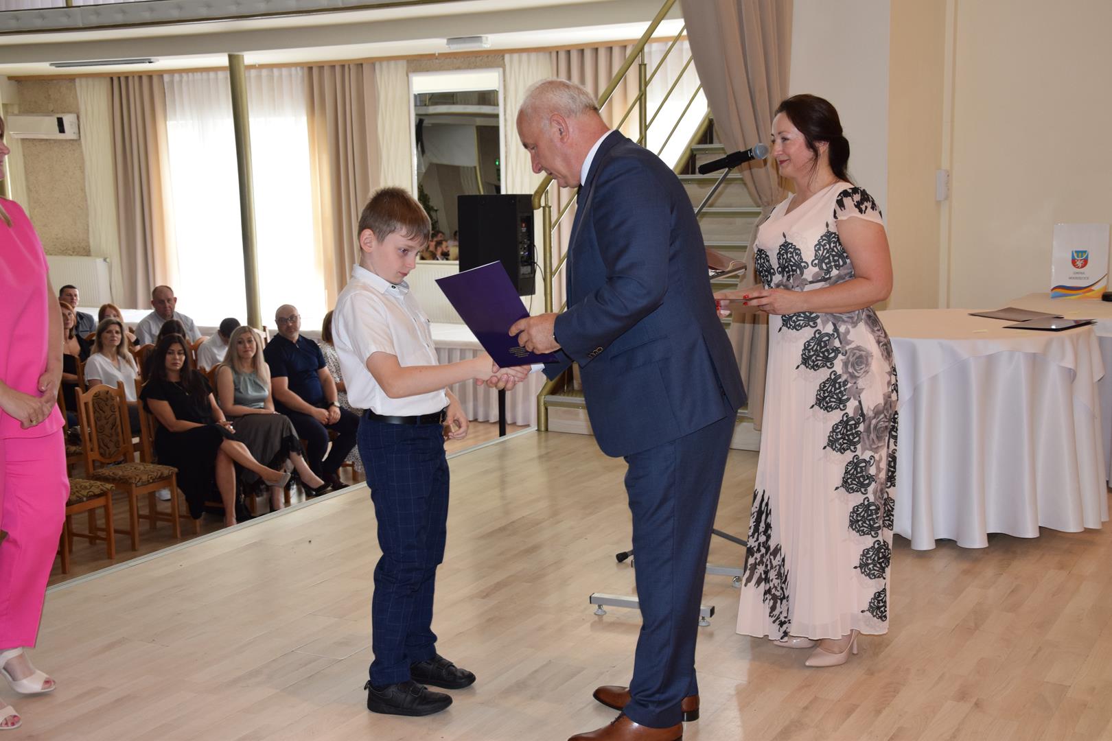 Zdjęcie przedstawia moment wręczenia dyplomów z okazji promocji ucznia zdolnego 2024