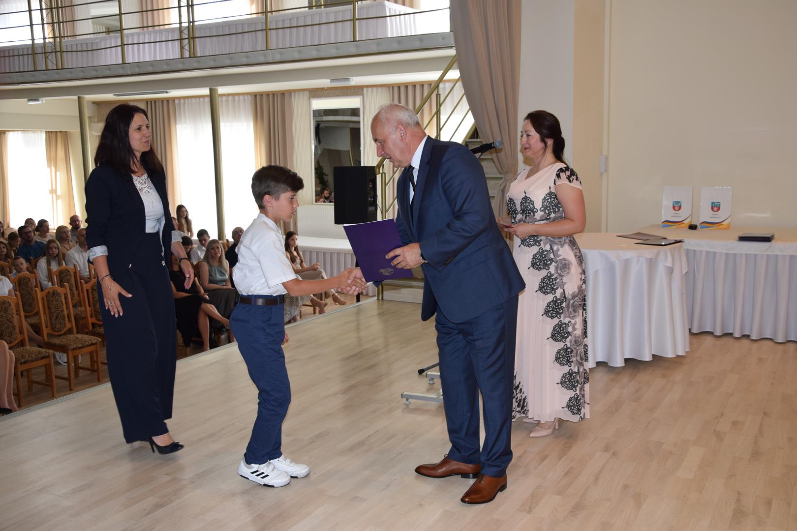 Zdjęcie przedstawia moment wręczenia dyplomów z okazji promocji ucznia zdolnego 2024