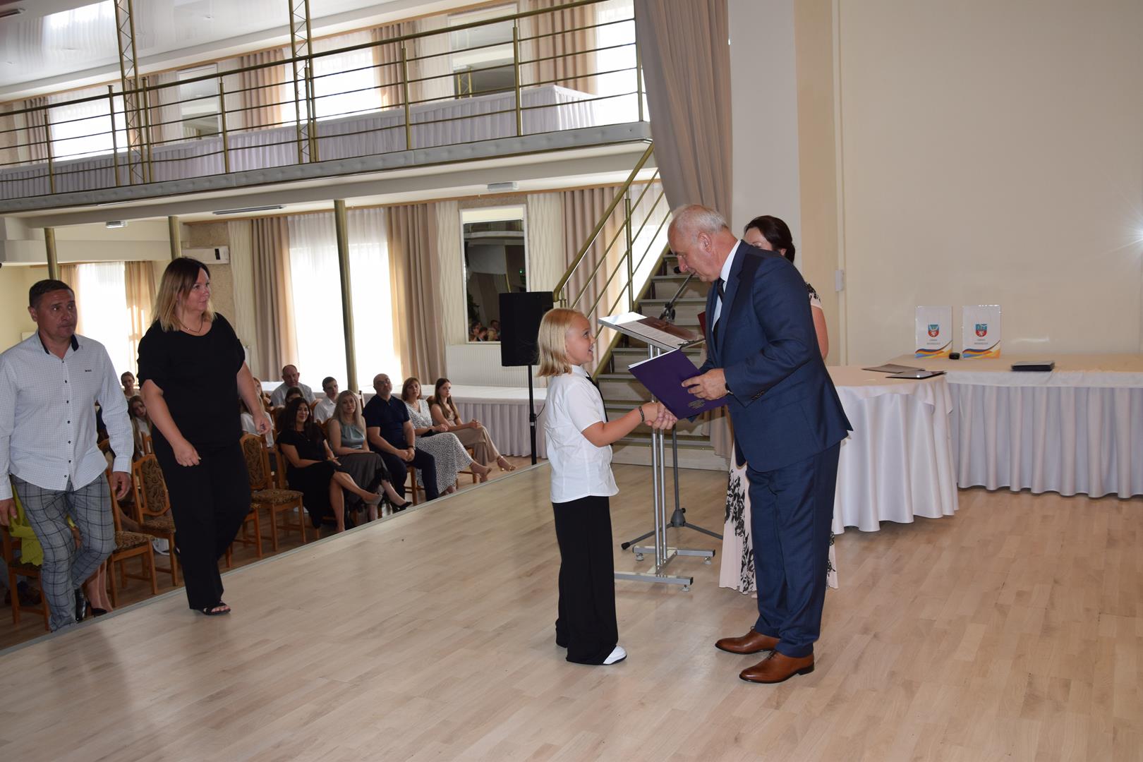 Zdjęcie przedstawia moment wręczenia dyplomów z okazji promocji ucznia zdolnego 2024