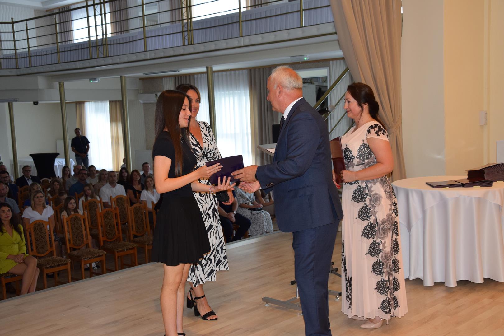 Zdjęcie przedstawia moment wręczenia dyplomów z okazji promocji ucznia zdolnego 2024