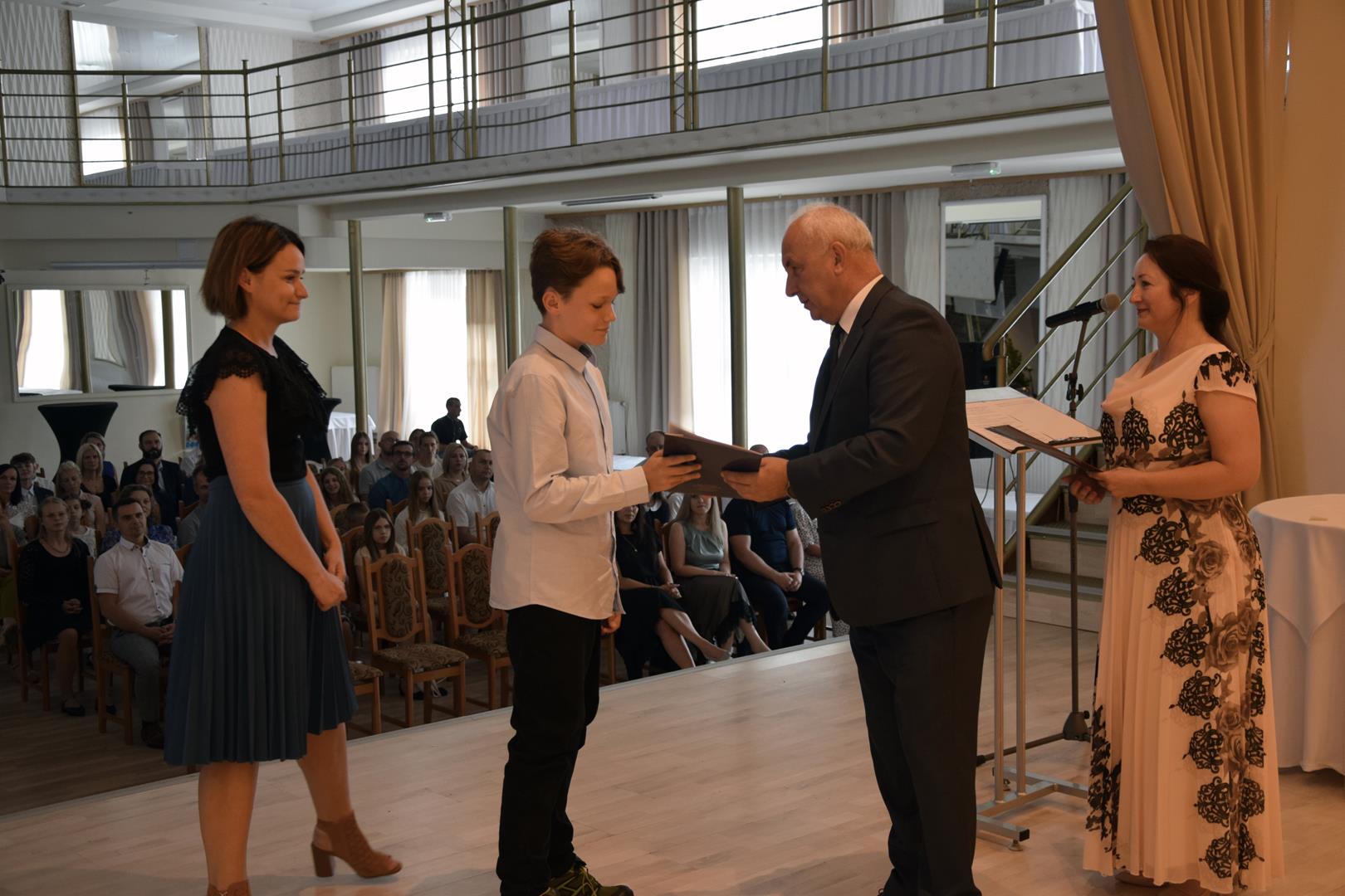 Zdjęcie przedstawia moment wręczenia dyplomów z okazji promocji ucznia zdolnego 2024