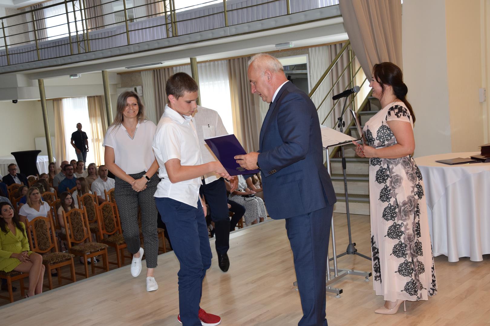 Zdjęcie przedstawia moment wręczenia dyplomów z okazji promocji ucznia zdolnego 2024