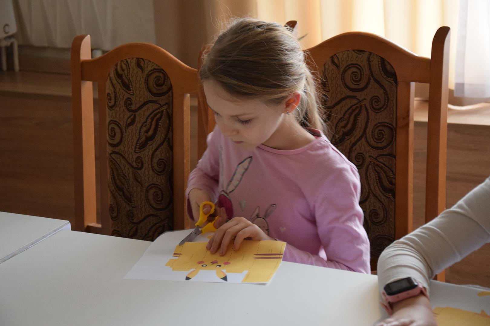 Zdjęcie przedstawiające dziewczynkę wycinającą pokemona z kartki papieru