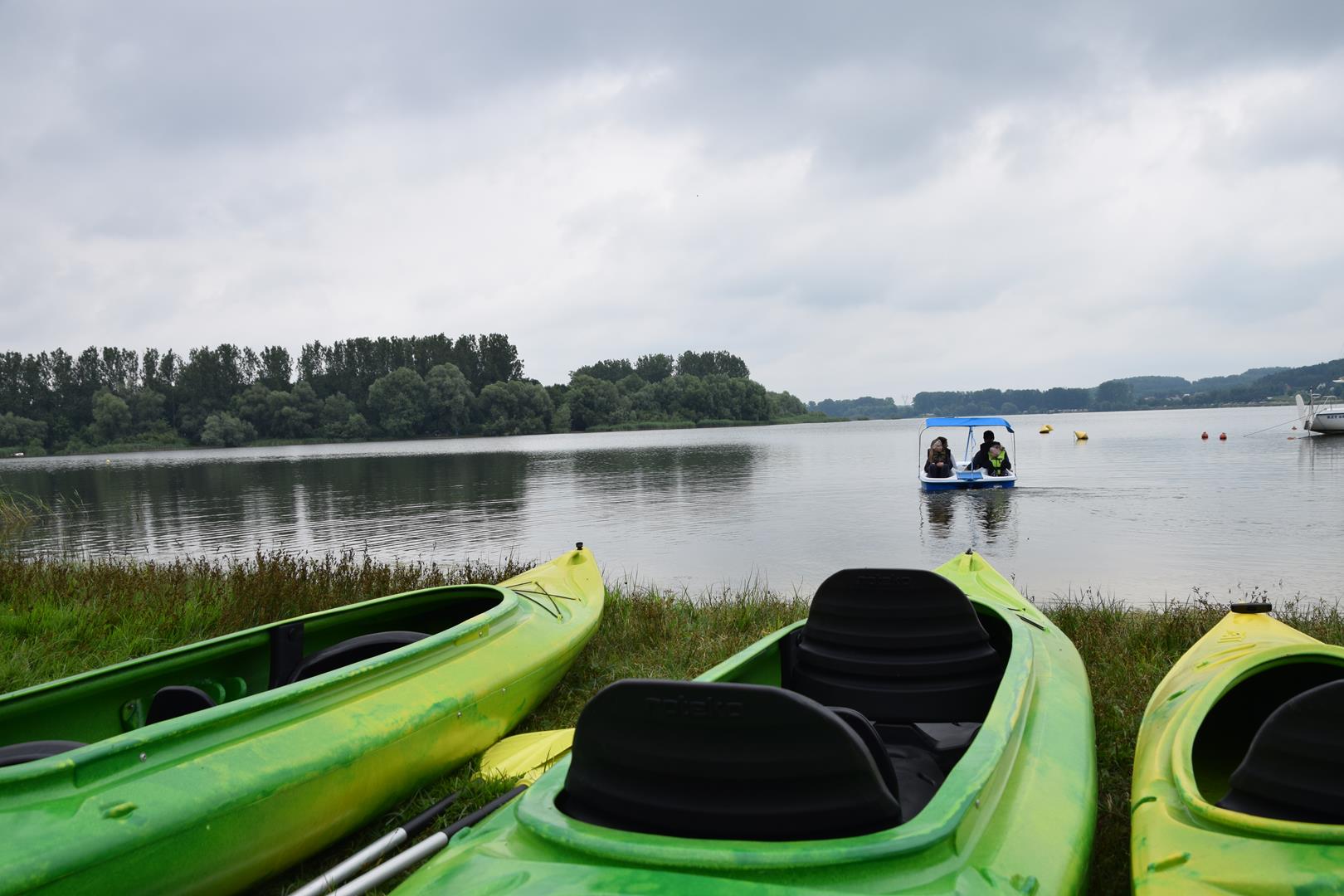 Zdjęcie przedstawiające uczestników wycieczki na rowerze wodnym oraz kajaki na brzegu zbiornika