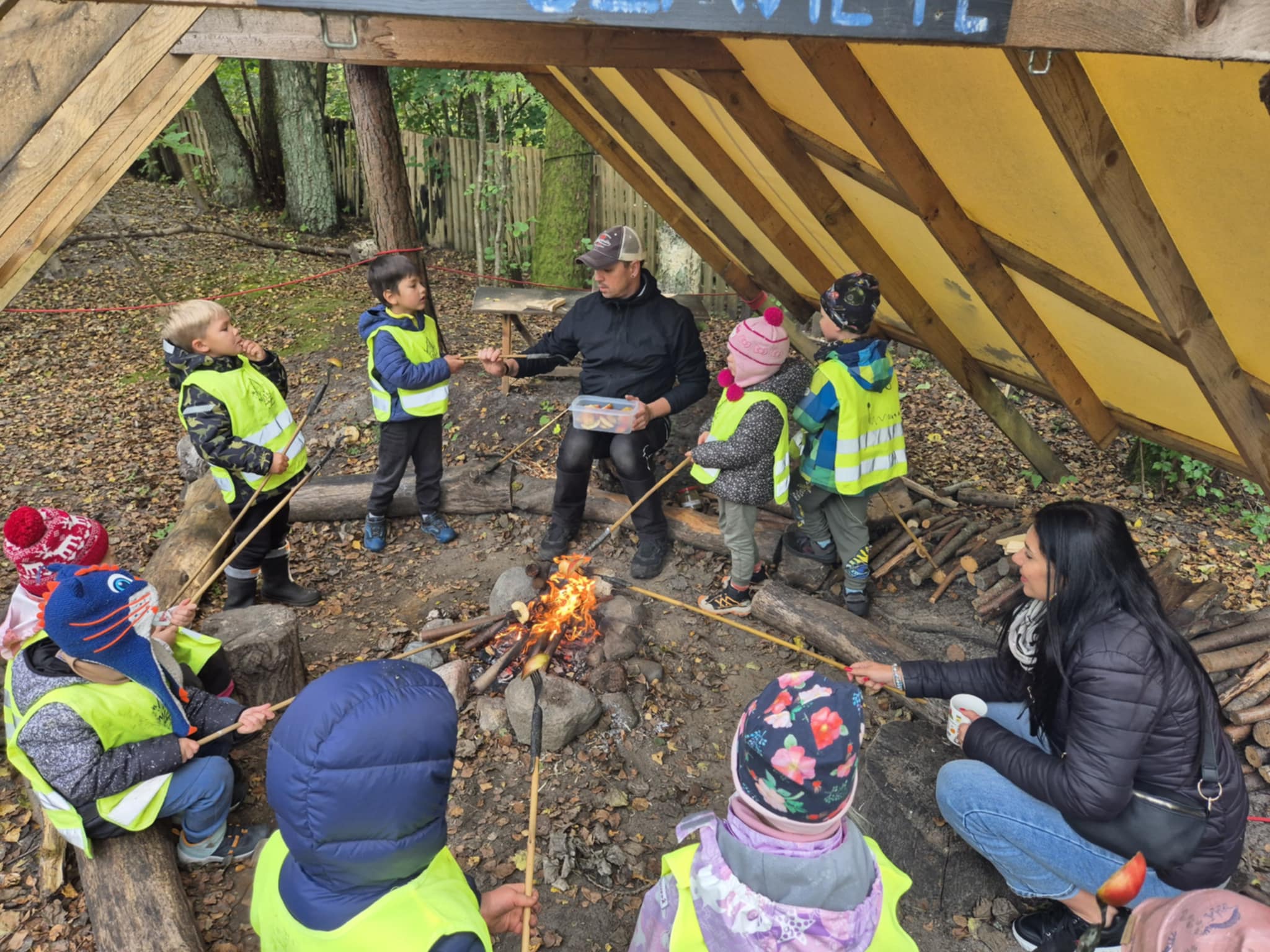 Zdjęcie przedstawia pieczenie kiełbasek przy ognisku